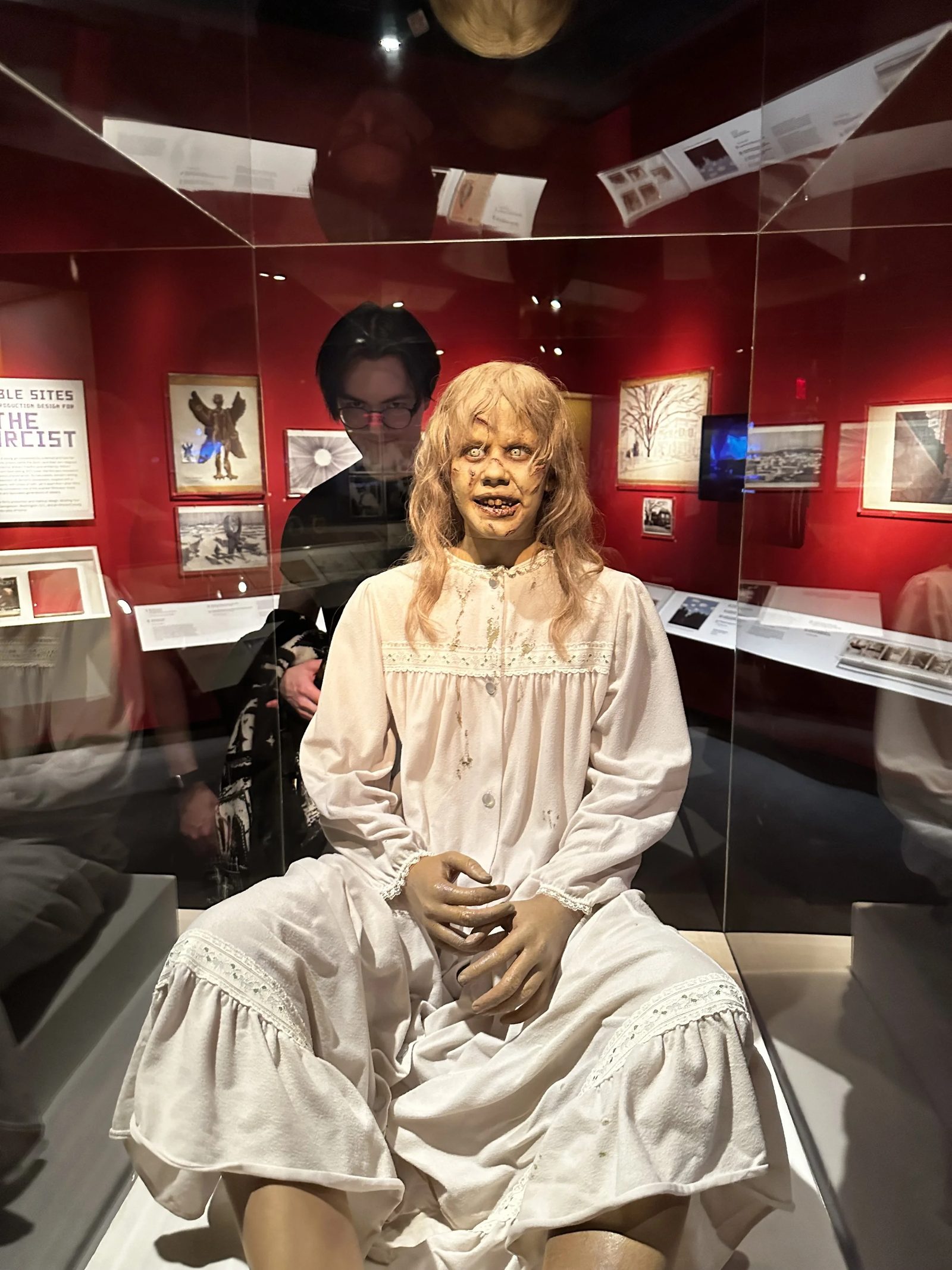 Wesley Thompson standing behind a museum display case holding the Regan MacNeil figure from The Exorcist
